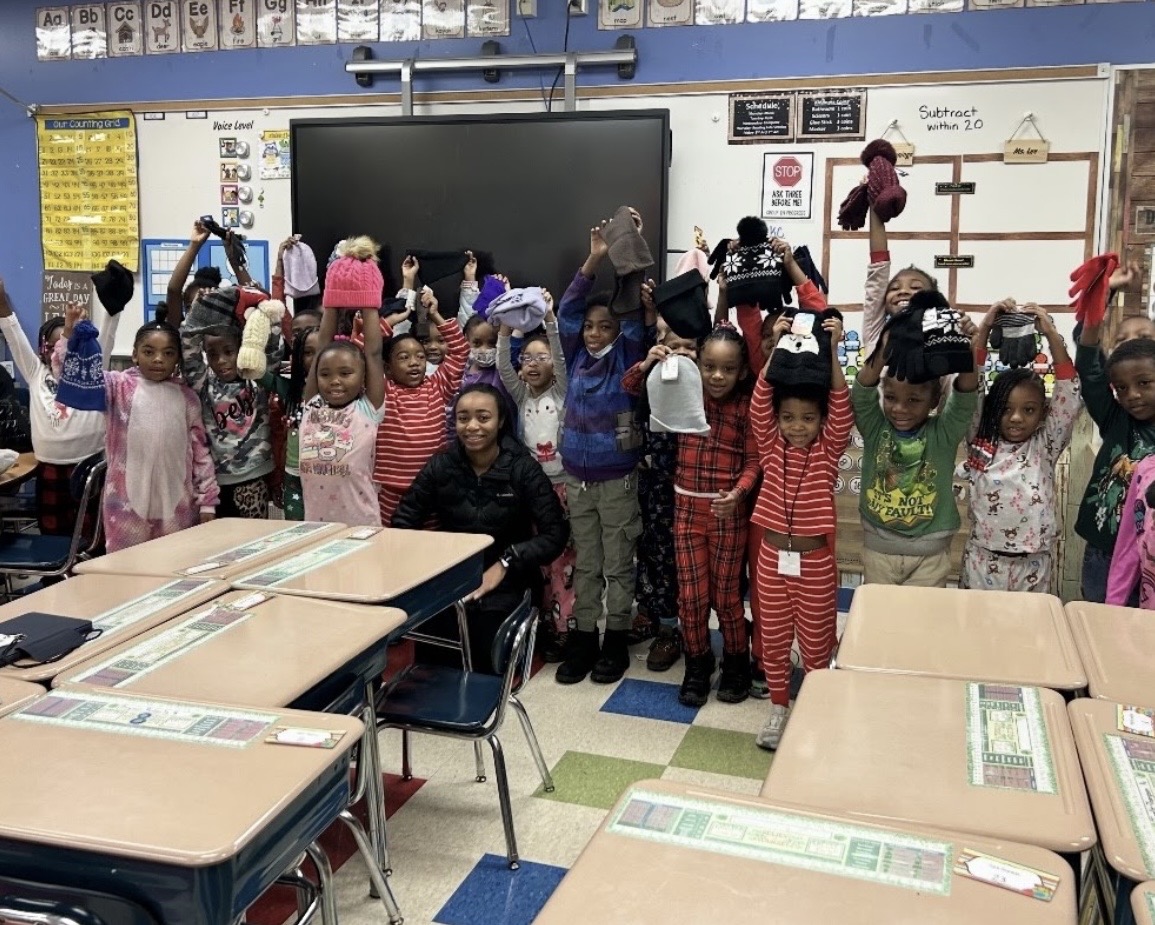 Students holding donated winter hats and gloves in a classroom.